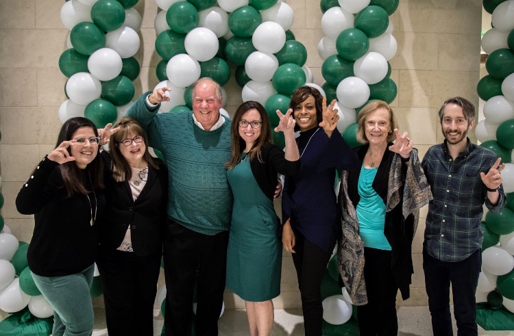 group of alumni in front of green and white balloons